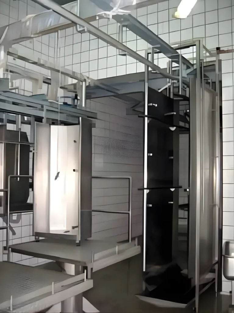 Spray apron washer and stainless-steel platforms in the clean zone of a meat-processing facility.